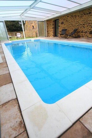 A swimming pool with a stone wall and a glass roof.