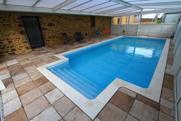 An indoor swimming pool with stone walls, a glass ceiling, and tiled flooring.