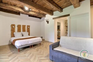 A bedroom with a wooden headboard, a bed with white bedding, a grey sofa, and a stone wall.