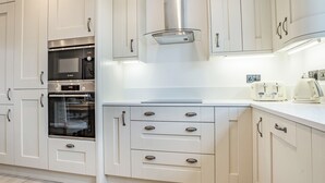 A modern kitchen with white cabinetry, stainless steel appliances, and a range hood. - Copper Beech Cottage - UK35892 (Ludchurch, near Narberth)