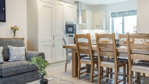 A modern living room with a sofa, dining table, chairs, and a potted plant. - Copper Beech Cottage - UK35892 (Ludchurch, near Narberth)