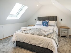 Um quarto com um claraboia, uma cama com manta estampada, duas mesas de cabeceira e uma cabeceira com travesseiro decorativo.