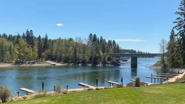 Vista junto al río con un puente, mesas de picnic y un espacio cubierto de césped.