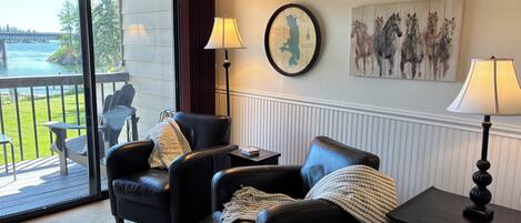 A room with two black leather chairs, a small table, a lamp, a framed map, and a painting of horses.