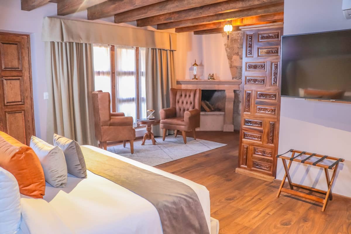A cozy room with a bed, two armchairs, a small table, and a fireplace.