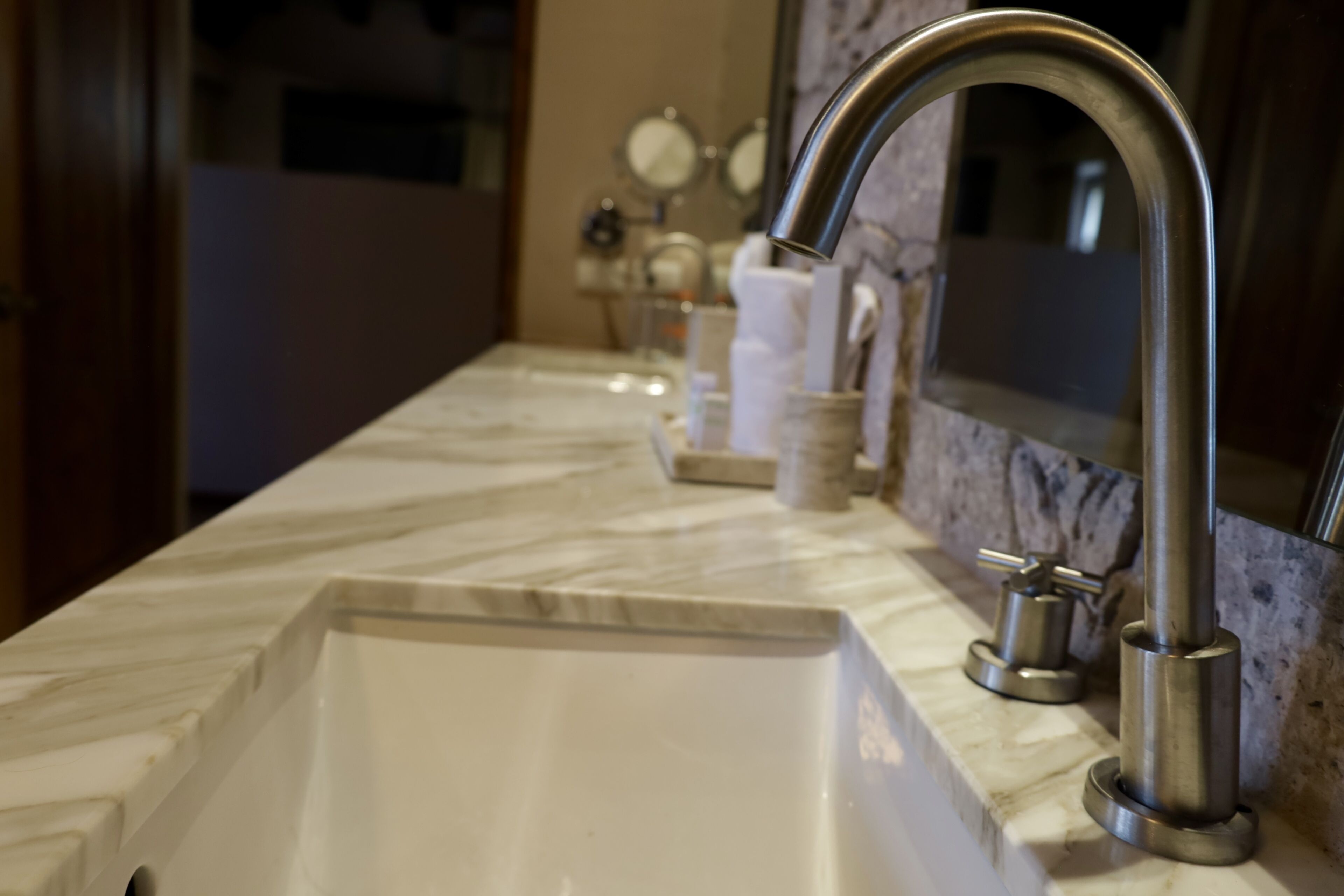 Un lavamanos de baño con un grifo moderno, un espejo y artículos de aseo en la encimera.