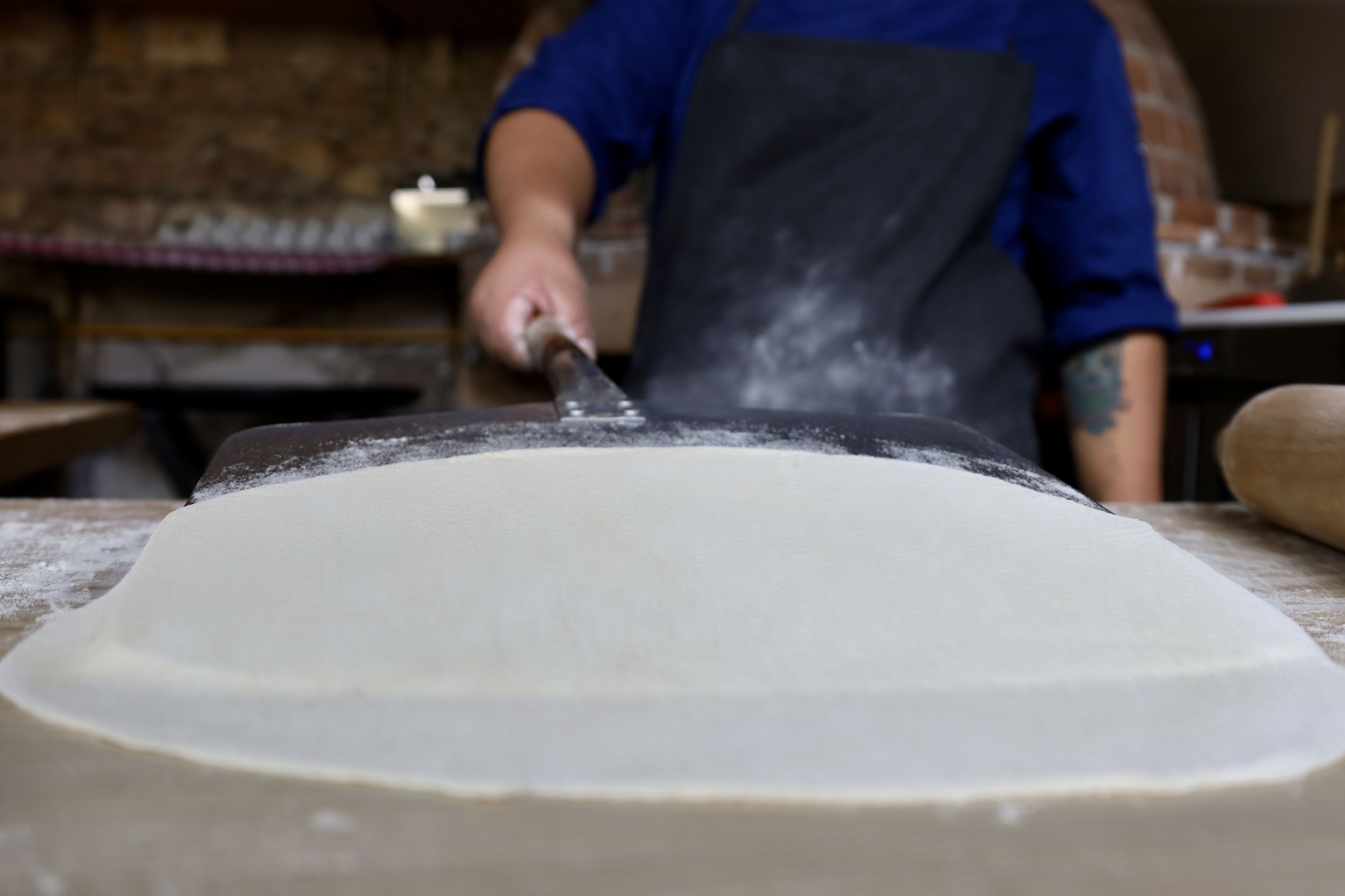 A person rolling out dough on a wooden surface in a kitchen setting.