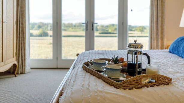 Een slaapkamer met een bed, een ontbijttafel, een koffiezetapparaat en uitzicht op een veld door de deur.