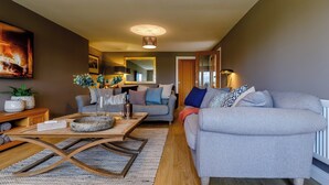 Een moderne woonkamer met een grijze bank, een houten salontafel en een televisie aan de linkerkant.