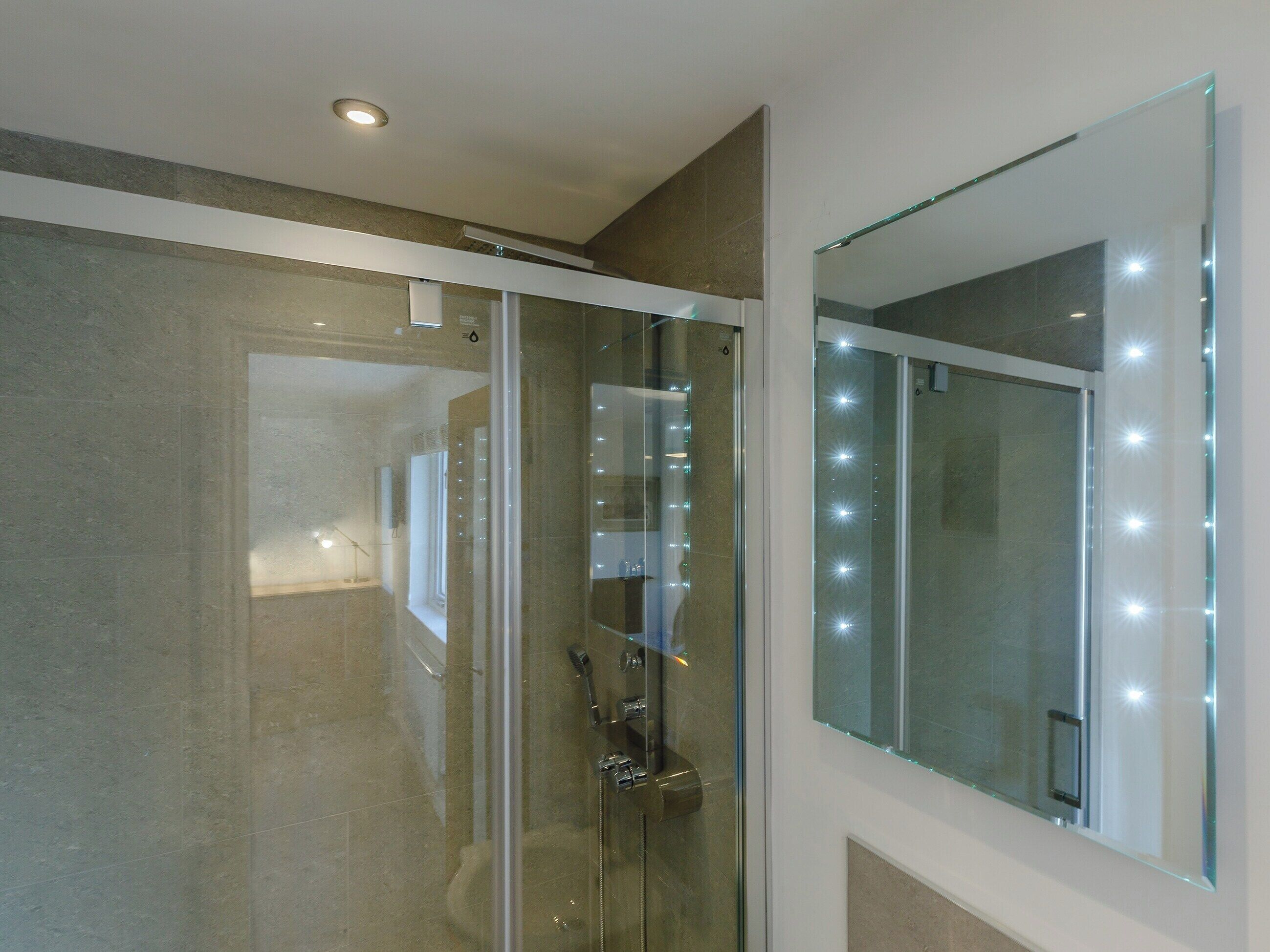 Une salle de bain moderne dotée d’une douche à parois de verre, d’un grand miroir et d’un éclairage encastré au plafond.