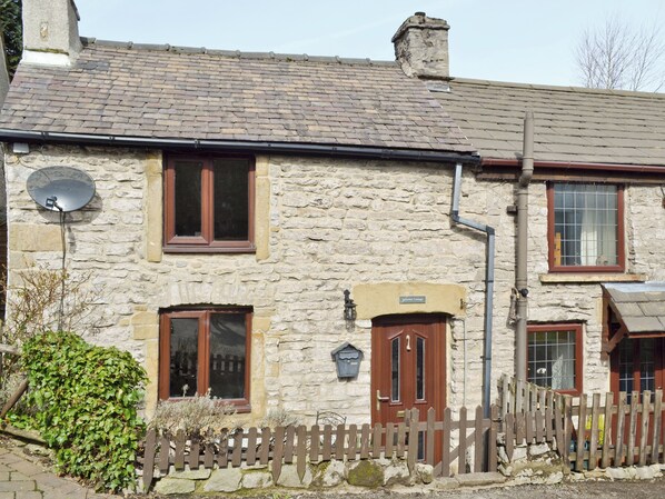A stone cottage with a wooden door, a satellite dish, and a small garden.