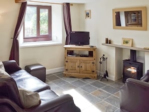 A living room with a sofa, a television on a wooden cabinet, a fireplace, and a window with curtains.
