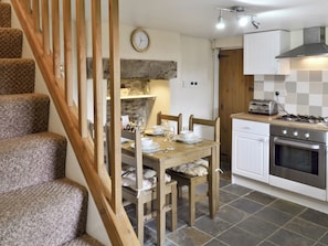 A kitchen with a wooden dining table set for two, a stove, and a clock on the wall.
