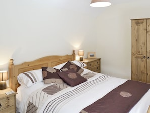 A neatly made bed with a wooden headboard, a bedside table with a lamp, and a wooden wardrobe.