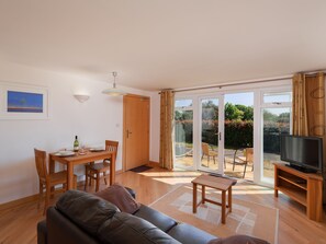 Una sala de estar con un sofá, una mesa de comedor con sillas, un televisor y un ventanal corredizo que da a un patio con mobiliario exterior.