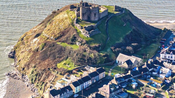 An aerial view of a coastal town with a prominent castle on a hill, surrounded by residential buildings. - Criccieth holiday apartment is a bolthole for two in a converted church. (Criccieth, near Llyn Peninsula)