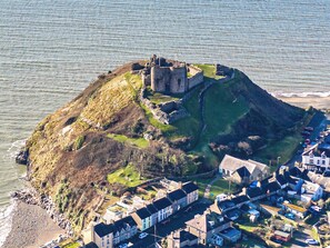 An aerial view of a coastal town with a prominent castle on a hill, surrounded by residential buildings.