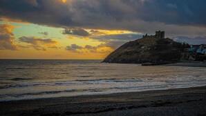 A coastal landscape with a castle on a hill, a beach, and the sea. - Criccieth holiday apartment is a bolthole for two in a converted church. (Criccieth, near Llyn Peninsula)