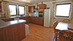Una cocina compacta con armarios de madera, horno empotrado, refrigerador y una zona de comedor con mesa y sillas.