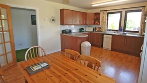 Una cocina compacta con armarios de madera, una mesa de comedor con sillas, un cesto de basura y una ventana con cortinas.