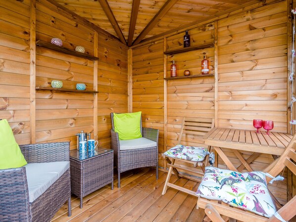 Une cabane en bois avec des meubles en osier, une table et des étagères remplies de bouteilles.