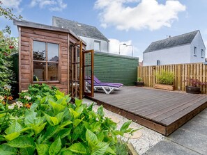 A wooden cabin with a deck, a green wall, and a white house in the background. - 1 bedroom accommodation in Pittenweem (Pittenweem)