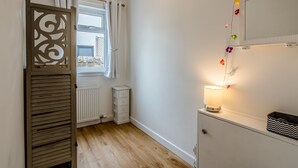 Et lille, godt oplyst rum med et vindue, en radiator og et skab med et spejl.