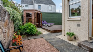 En lille baghave med træterrasse, siddeområde og en have med stedmoderblomster.