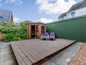 Une terrasse en bois avec deux chaises longues, une petite structure en bois dotée de portes vitrées et un mur végétal.