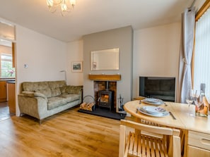 A cozy living room with a sofa, a fireplace, a TV, and a dining table set for two. - 1 bedroom accommodation in Pittenweem (Pittenweem)