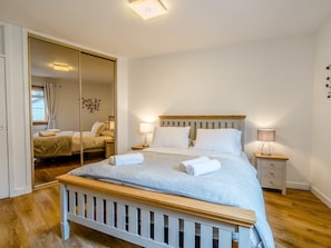 A bedroom with a wooden bed, two bedside tables, a mirror, and a window with curtains. - 1 bedroom accommodation in Pittenweem (Pittenweem)