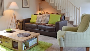 Una sala de estar con un sofá de cuero marrón, un sillón verde, una mesa de centro de madera y una escalera con barandillas blancas.