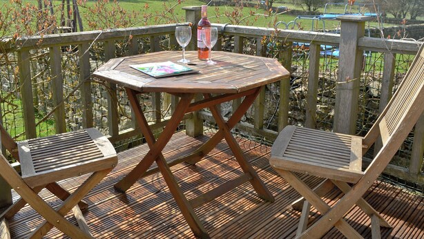 Una terraza de madera con una mesa redonda y dos sillas, con vista a un paisaje pintoresco.