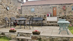A stone building with a tiled roof, outdoor seating with metal chairs and tables, and a clock on the wall.