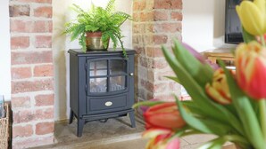 A traditional black wood-burning stove with a glass door, a potted fern on top, and a brick wall.