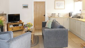 A living room with a grey sofa, a coffee table, a TV stand with books, and a vase of flowers.