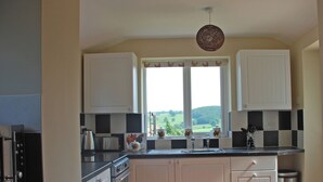 A kitchen with white cabinets, a black countertop, a window with a view of the countryside, and a hanging light fixture. - 2 bedroom accommodation in Youlgreave near Bakewell (Youlgreave near Bakewell)