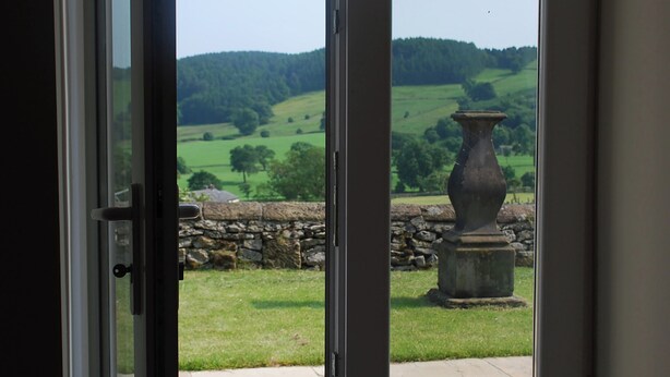 A view through a glass door of a stone wall and a large vase, with a green landscape and hills in the background. - 2 bedroom accommodation in Youlgreave near Bakewell (Youlgreave near Bakewell)