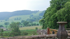 A stone wall with a wooden fence and a stone pillar in a rural landscape with rolling hills and trees. - 2 bedroom accommodation in Youlgreave near Bakewell (Youlgreave near Bakewell)