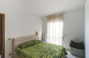 Quarto com cama, radiador, mala e janela com cortinas.