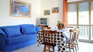 Ein Wohnzimmer mit einem blauen Sofa, einem Esstisch mit einem Tischlein in Punkteoptik und einem Fernseher auf einem Lowboard.