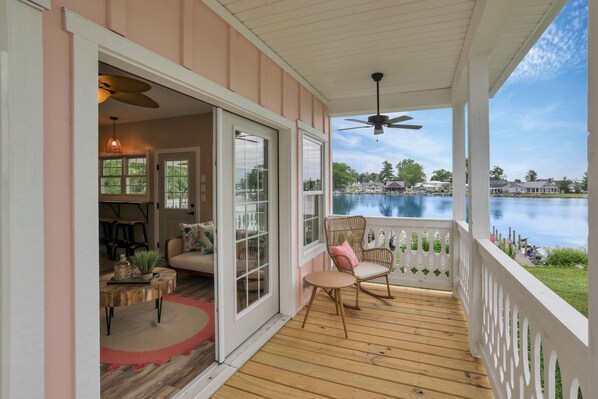 A covered porch with a view of a lake, wooden flooring, wicker chairs, and a dining area with a table and chairs.