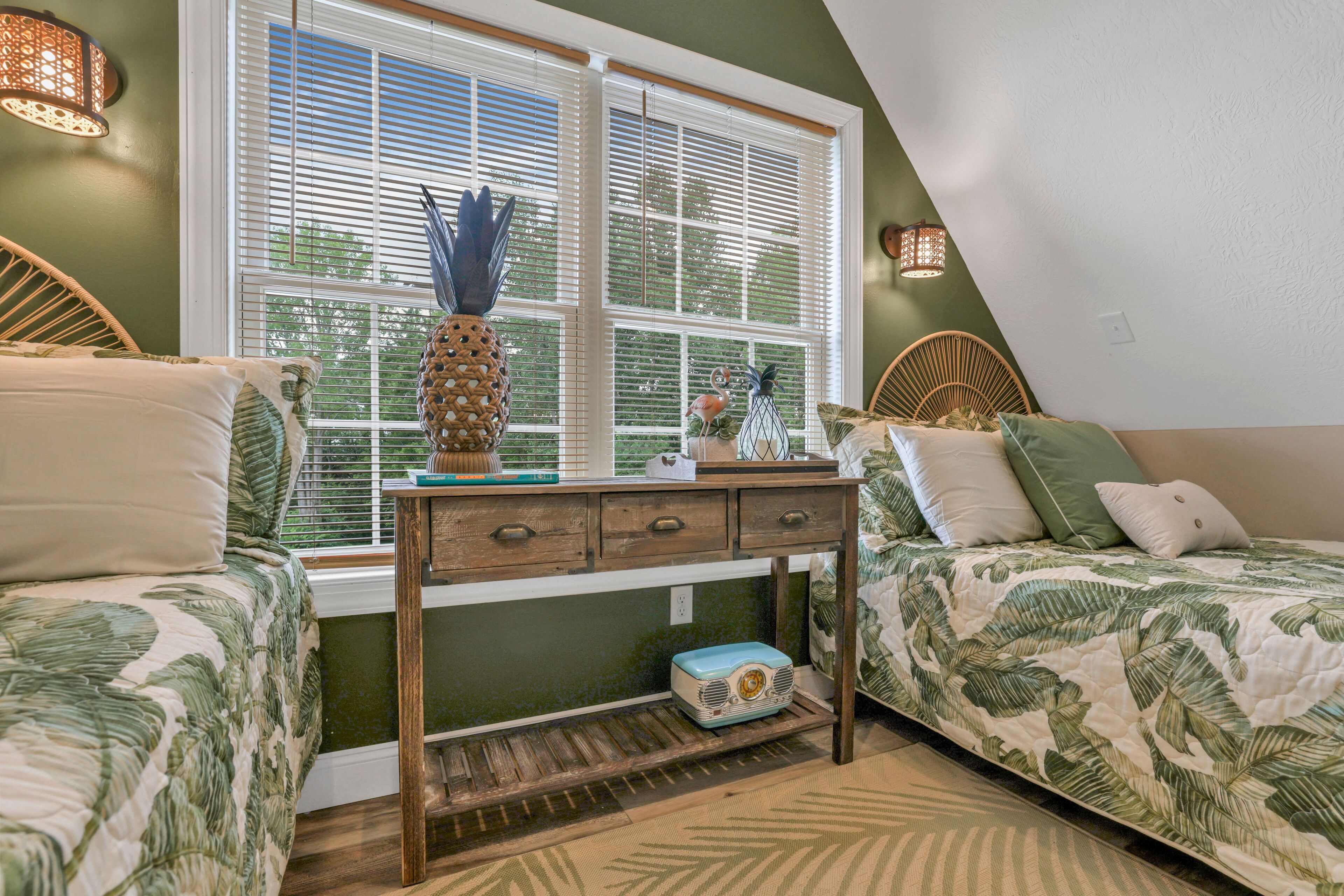 A bedroom with two beds, a nightstand, a window with blinds, and a decorative vase.