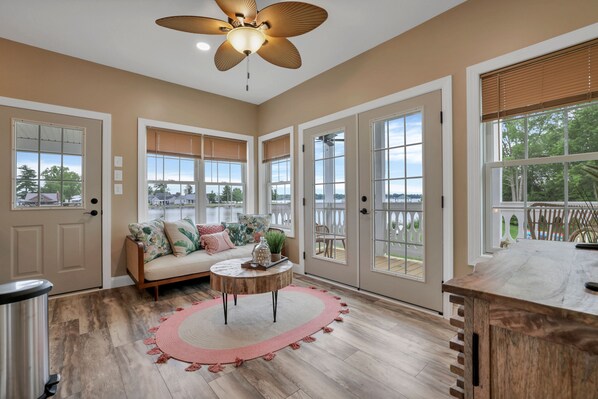 A spacious room with a large sliding glass door leading to a deck, a wooden floor, a round coffee table, and a ceiling fan.