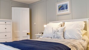 Quarto com cama, mesinhas de cabeceira brancas, cômoda e um quadro na parede.
