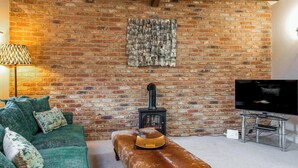 A cozy living room with a brick wall, a green sofa, a wooden bench, a television, and a fireplace.