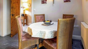 A dining area with a round table, four wicker chairs, a bowl of fruit, and wall-mounted light fixtures.