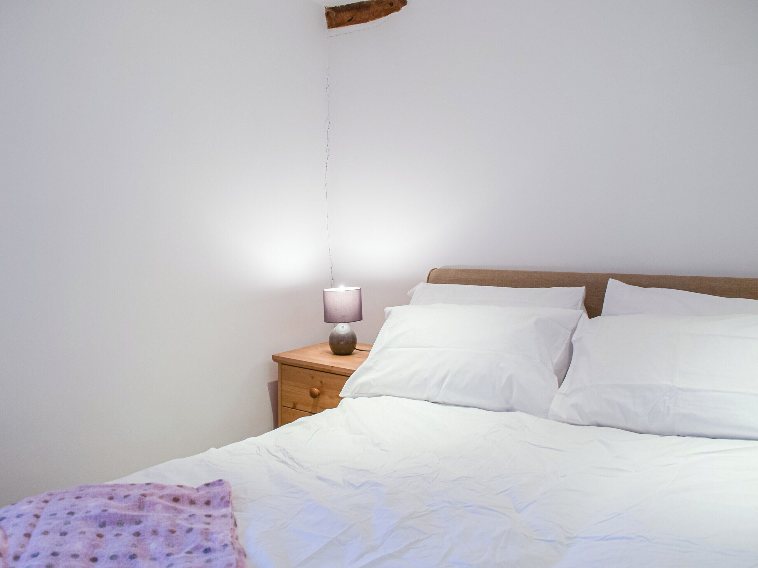 A neatly made bed with white linens, a wooden nightstand with a lamp, and a wooden headboard.