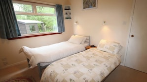 A bedroom with two single beds, a window with curtains, a small shelf with decorative items, and a door. - 2 bedroom accommodation in Portree, Isle of Skye (Portree, Isle of Skye)
