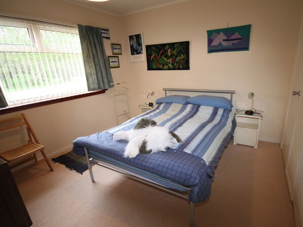 Een slaapkamer met een bed, een nachtkastje, een stoel, een raam met gordijnen en wanddecoratie.